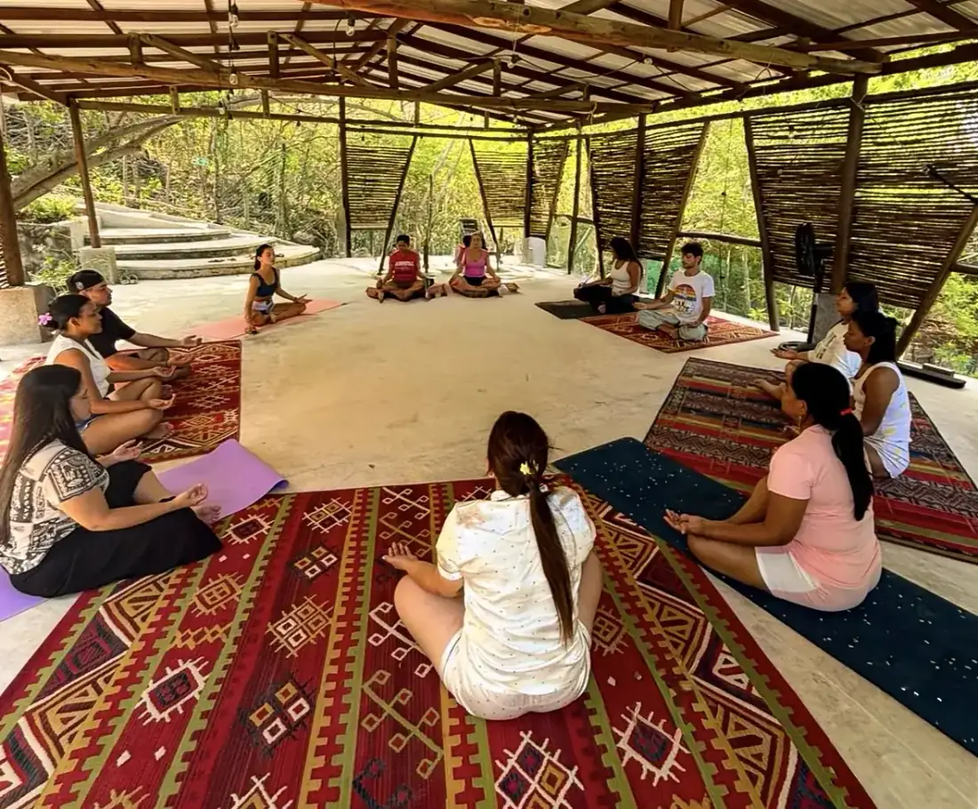 Clase de yoga en grupo, sentados en ronda sobre alfombras bajo un techo de madera