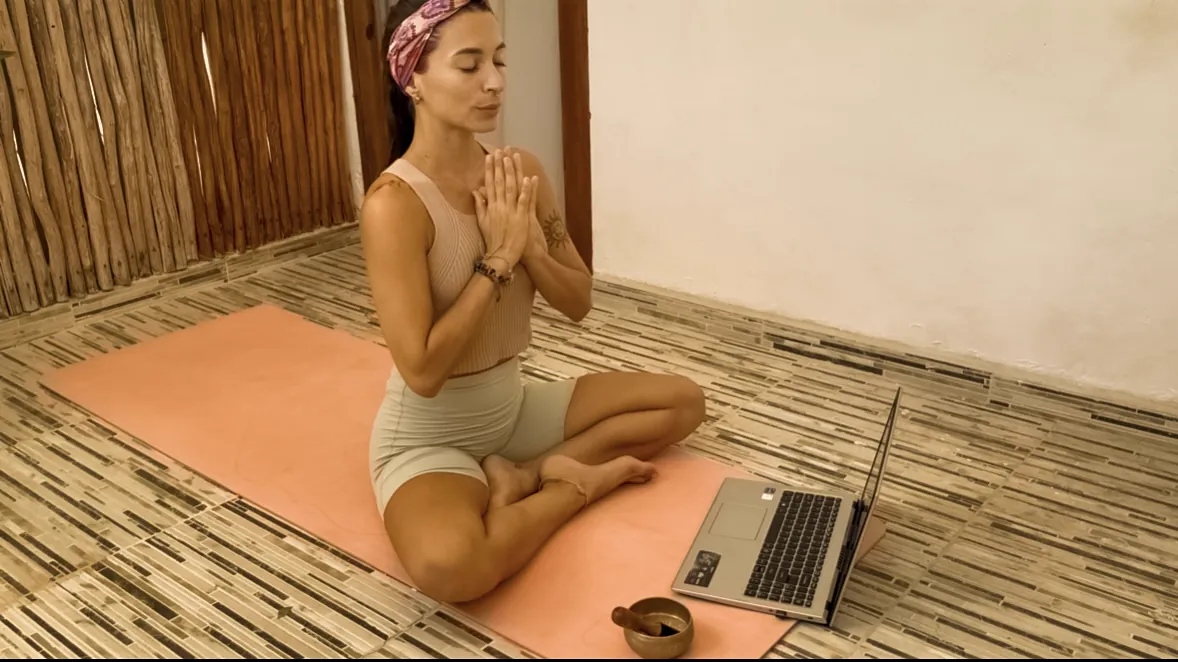 Flori meditando con las manos en el pecho, con la computadora lista para una clase online