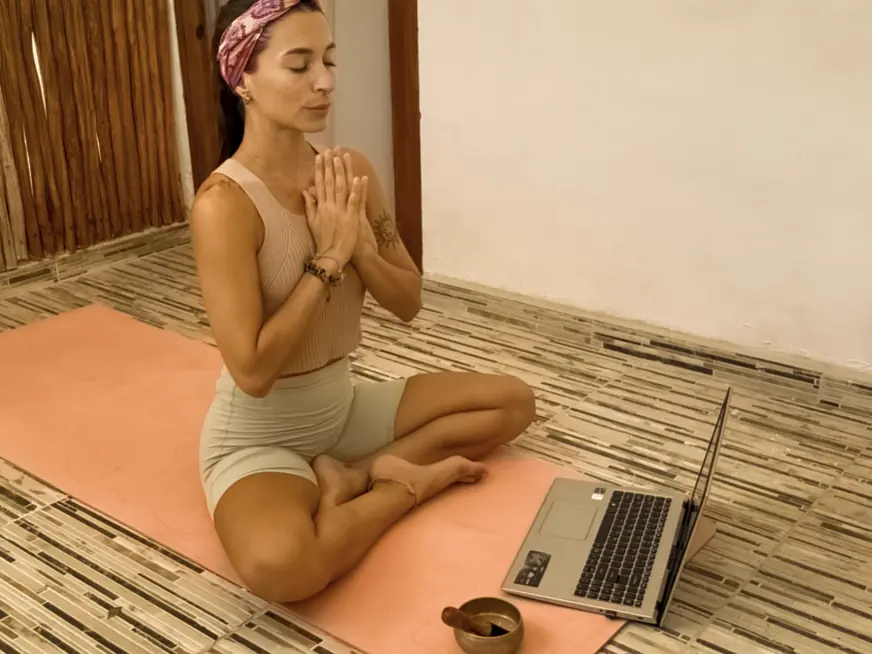 Flori meditando en su esterilla, con la computadora lista para una clase online